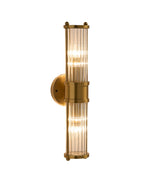 Brimsley II Wall Sconce illuminated, featuring a vertical brass body with ripple-textured clear glass panels, shown on a white background highlighting its elegant glow and elongated form.