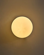 Round wall sconce with an opaque white glass globe, illuminated and mounted on a wall.