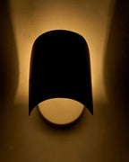 Wall-mounted sconce with a curved black metal shade, illuminated and casting warm light upward and downward.