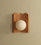 Clemence wall sconce with oak wood backplate and white glass globe, mounted on a neutral wall.