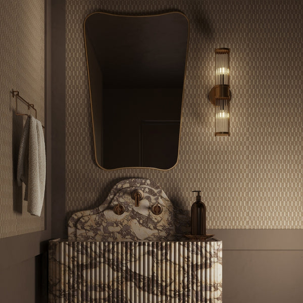 Butterfly Mirror with an irregular, wing-inspired shape mounted above a wall-mounted sink, styled with a vertical wall light, towel hook, and minimal accessories in a softly lit bathroom.