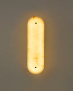 Vertical marble wall sconce mounted on a wall, illuminated and casting a soft, warm ambient glow.
