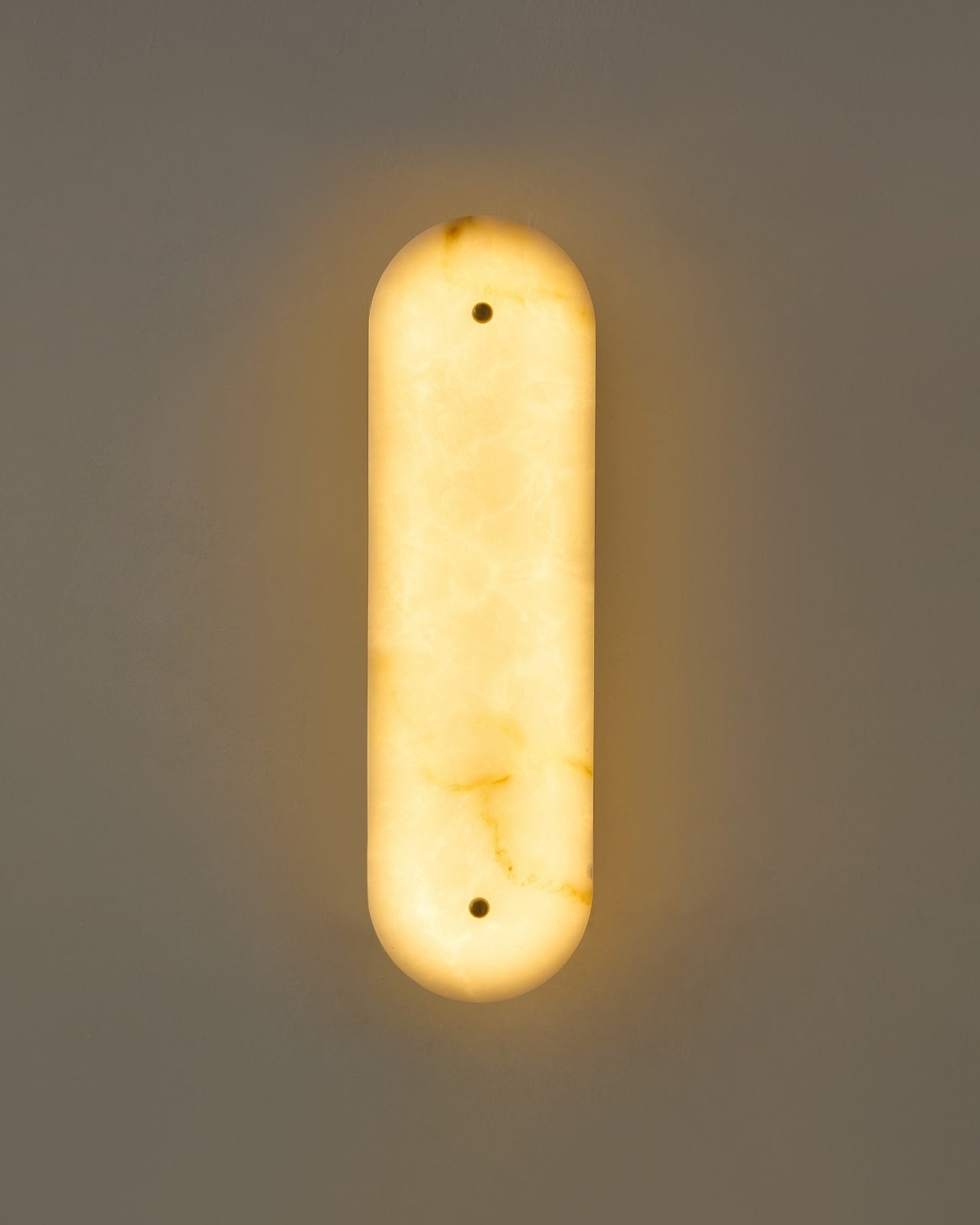 Vertical marble wall sconce mounted on a wall, illuminated and casting a soft, warm ambient glow.