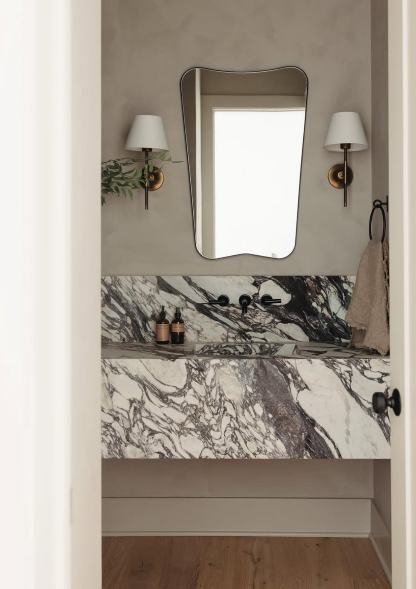 Elegant bathroom with a statement marble sink, butterfly shaped mirror, and dual wall sconces. Minimalist decor with a soft, tranquil ambiance.