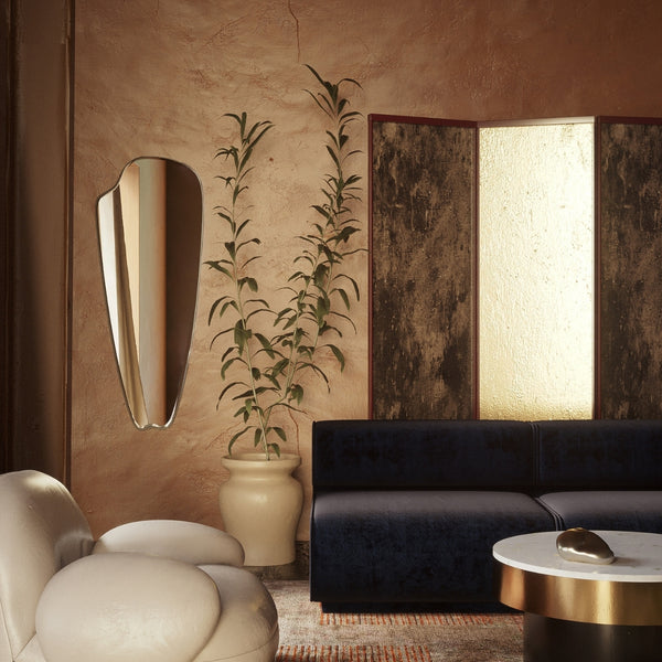 Horizontally mounted frameless wall mirror with an elongated organic shape, displayed above a light-colored sofa in a minimalist interior.