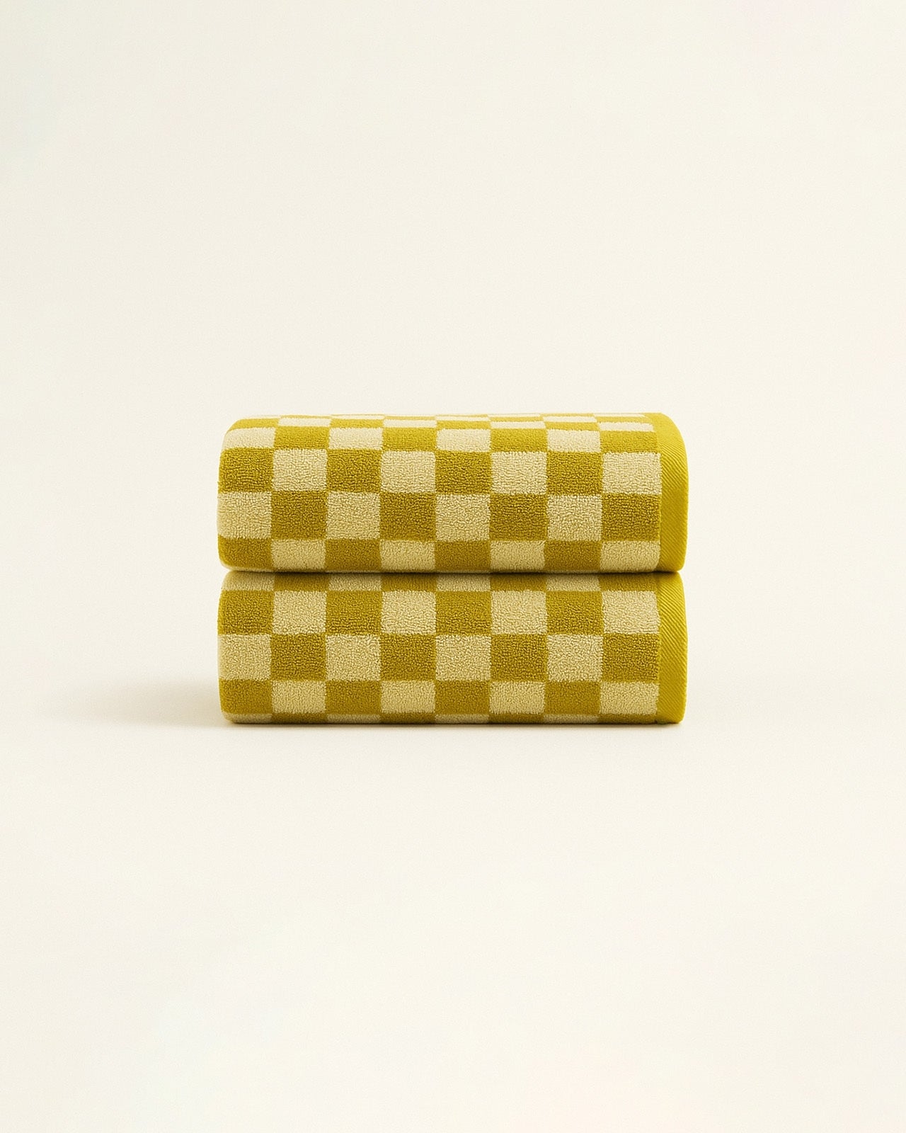 Two mustard and white checkered towels neatly rolled and stacked, showcasing the geometric pattern and soft terry texture on a neutral background.