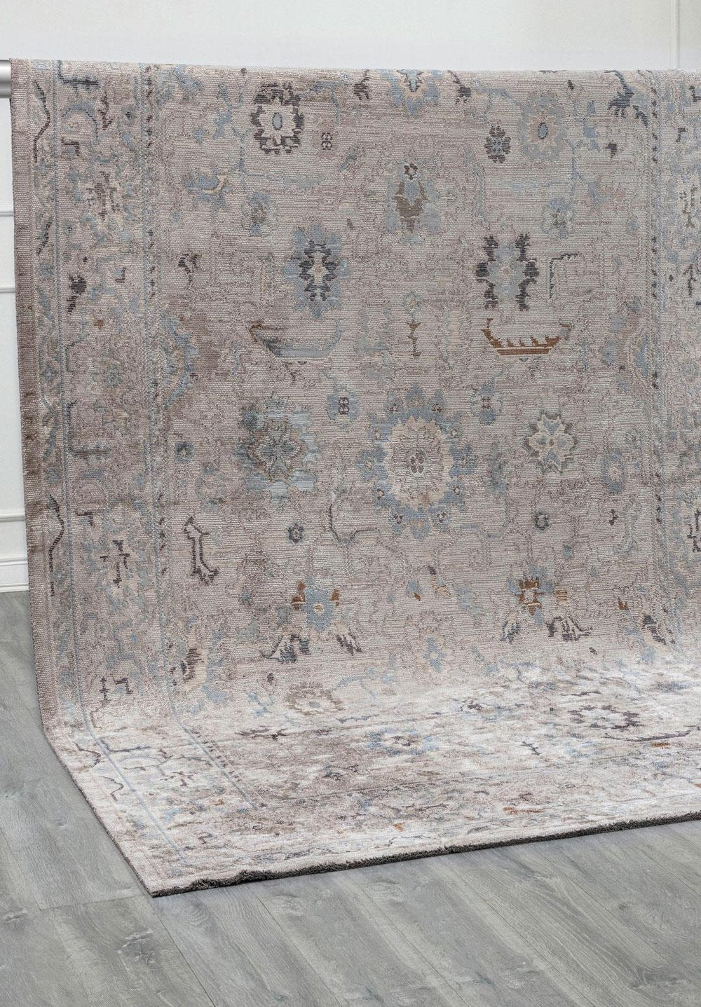 Flat-woven rug with a muted gray and blue pattern, shown partially rolled on a light wood floor.