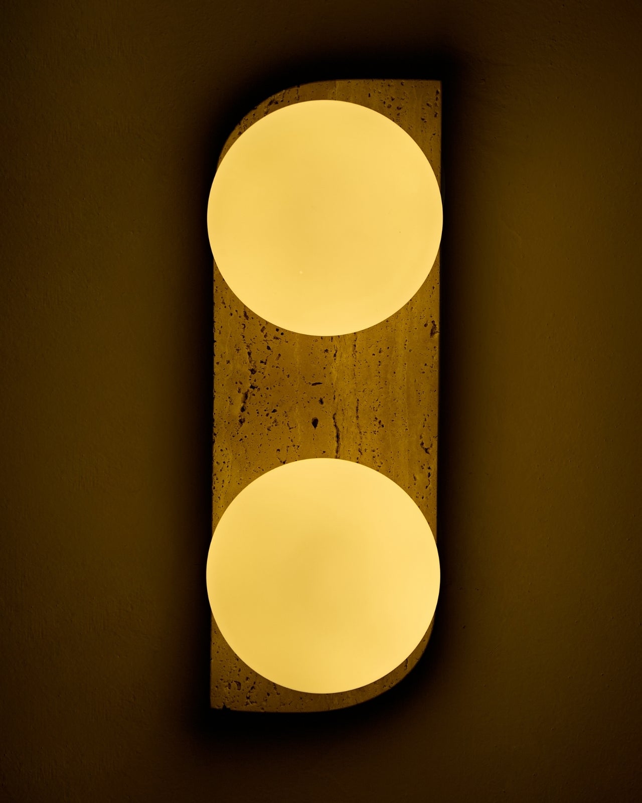 Travertine wall sconce illuminated with two warm white round glass globes mounted vertically on a wall.