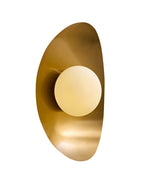 Wall-mounted light with a circular opaque white glass globe centered on an elongated, curved brass backplate, shown against a white background.