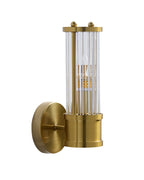 Wall-mounted brass sconce with a cylindrical clear ribbed glass shade, shown unlit against a white background, with the bulb visible inside.
