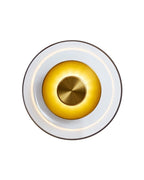 Wall-mounted brass sconce with a circular clear glass shade and a central brass disc, shown lit against a white background, emitting a soft warm light.