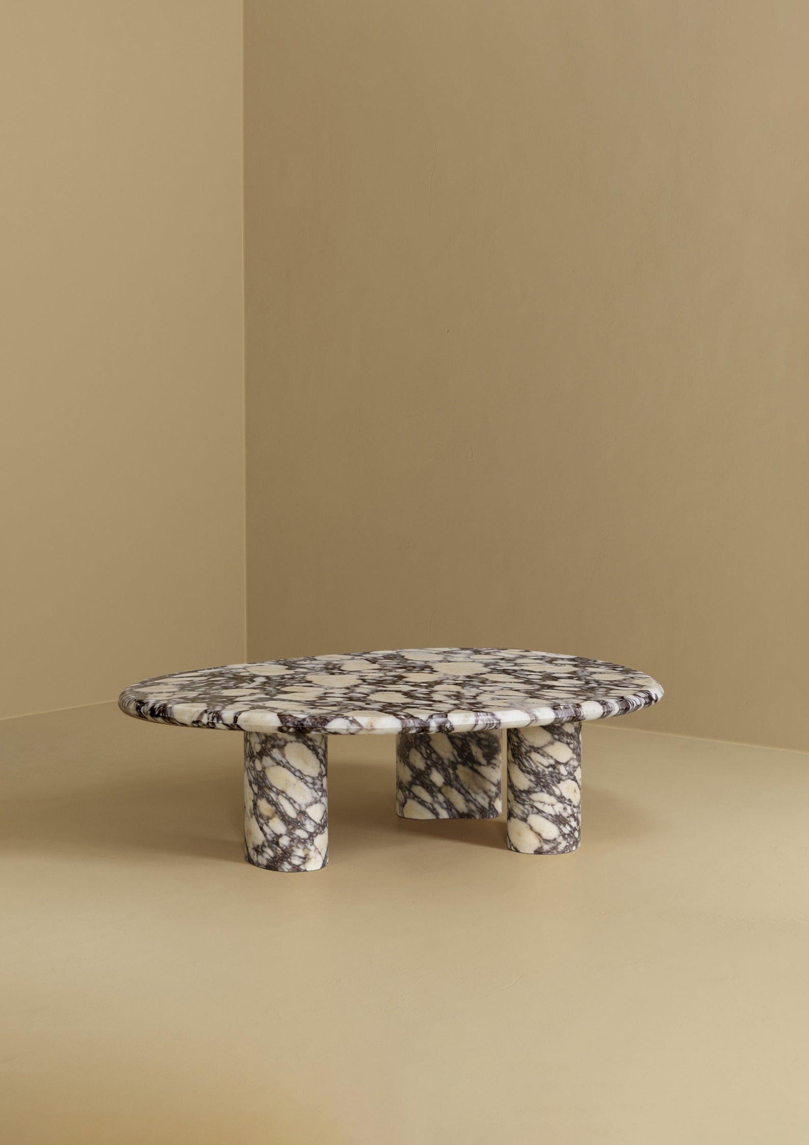 A low coffee table with an organic-shaped marble top and three rounded marble legs, placed against a plain wall and floor.