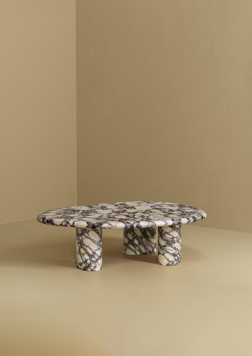 A low coffee table with an organic-shaped marble top and three rounded marble legs, placed against a plain wall and floor.