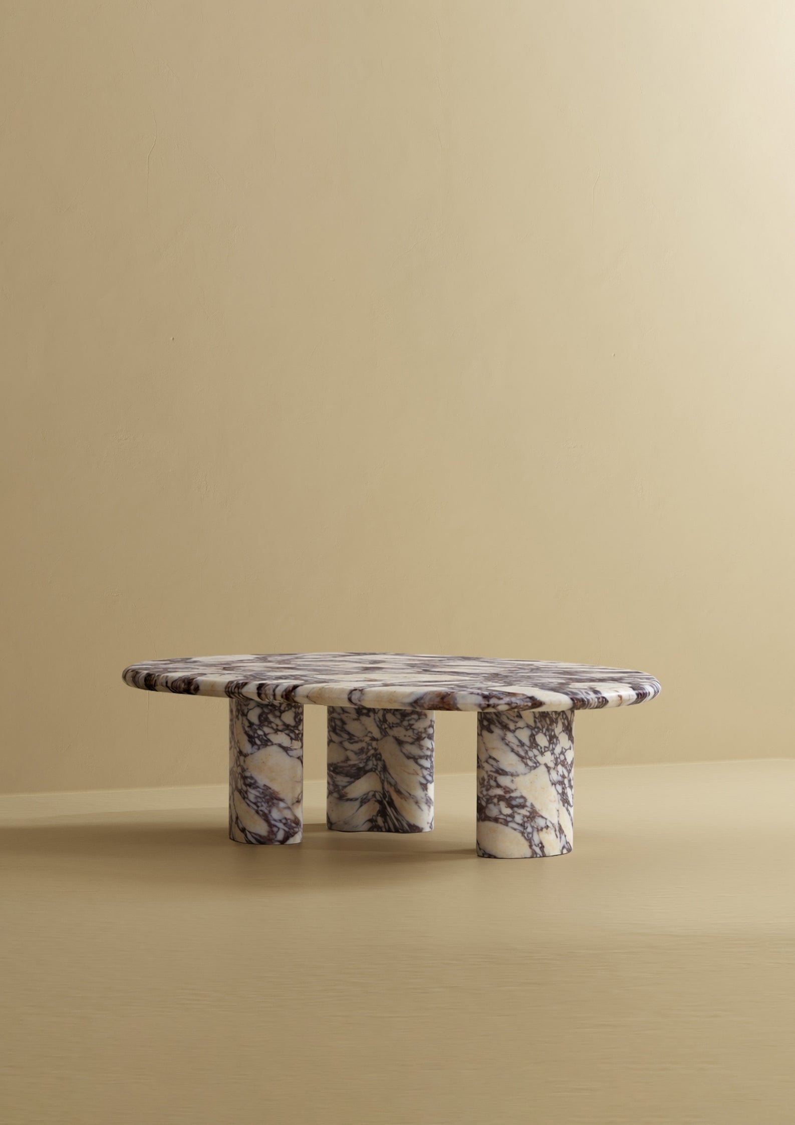 A low coffee table with an organic-shaped marble top and three rounded marble legs, photographed against a plain wall and floor.