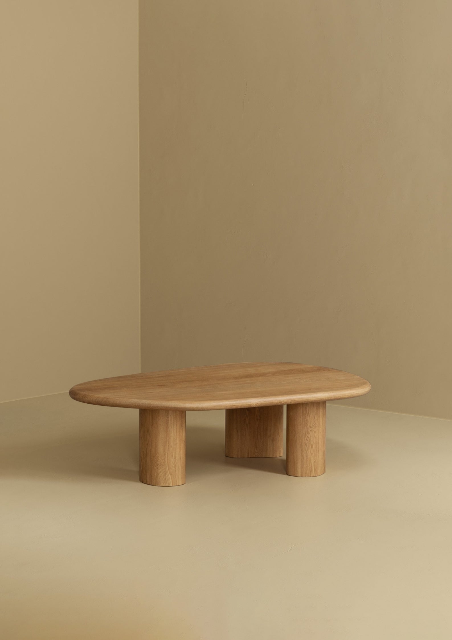 A low coffee table with an organic-shaped smooth top and three rounded legs, made of natural wood, positioned against a plain wall and floor.