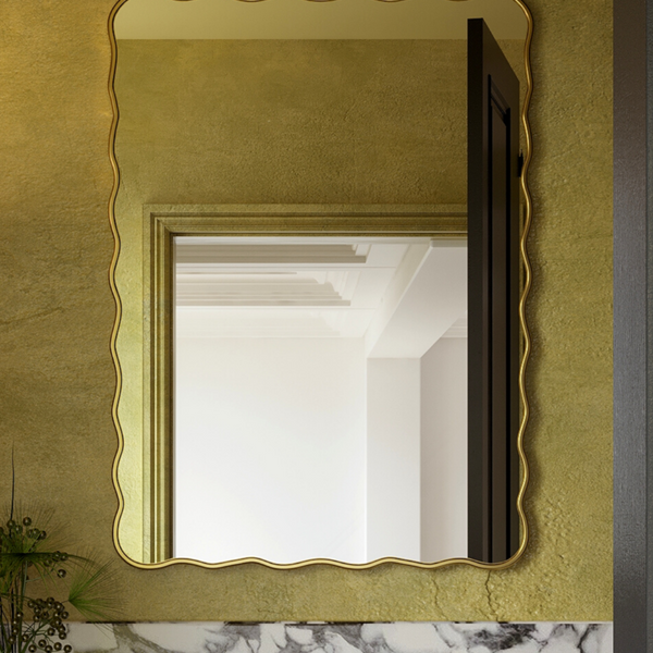 Rectangular wall mirror with a softly wavy gold frame mounted on a textured wall above a marble vanity.