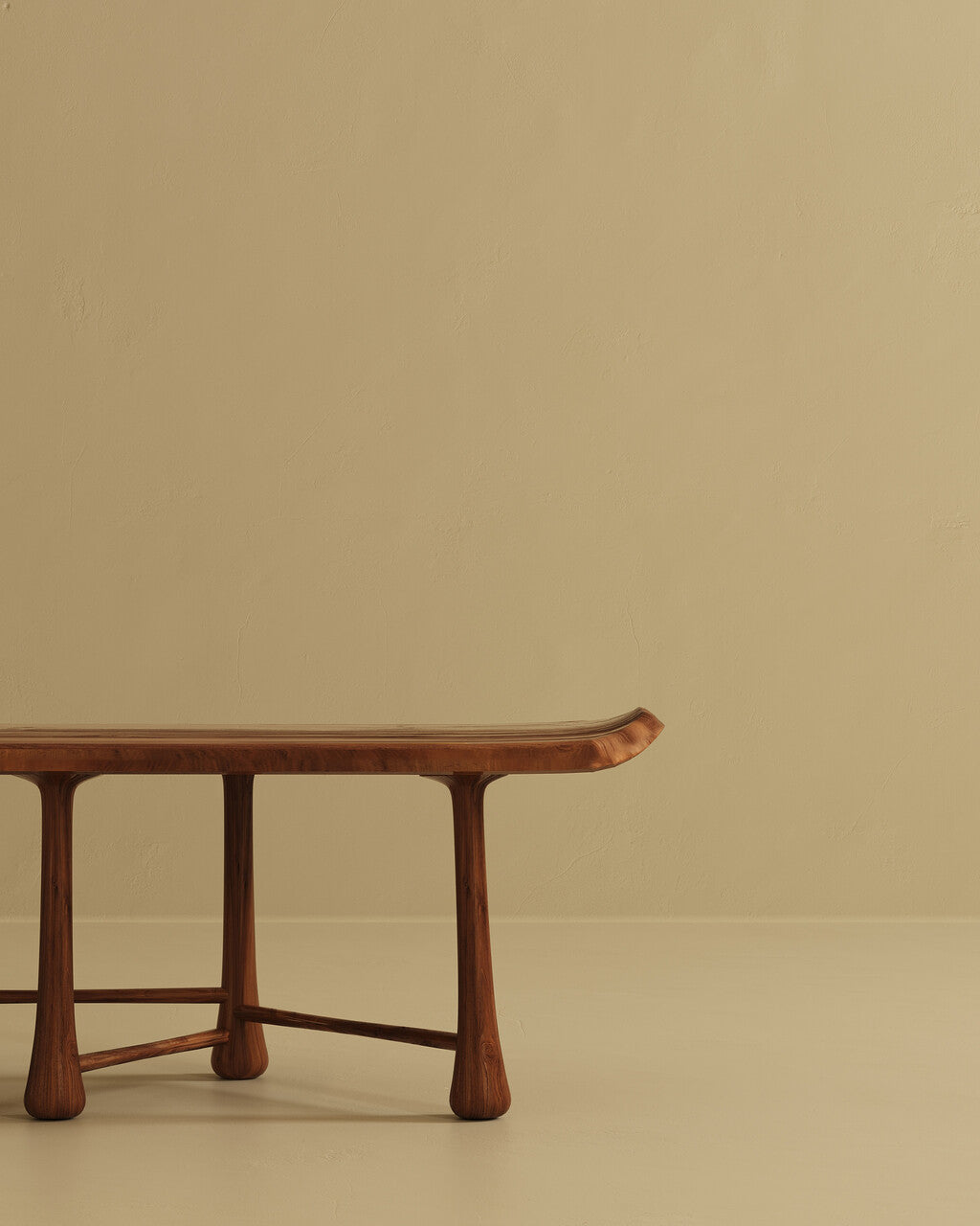 A close-up view of one end of a wooden bench, showing the smooth tabletop edge, rounded legs, and connecting support bars against a plain wall and floor.