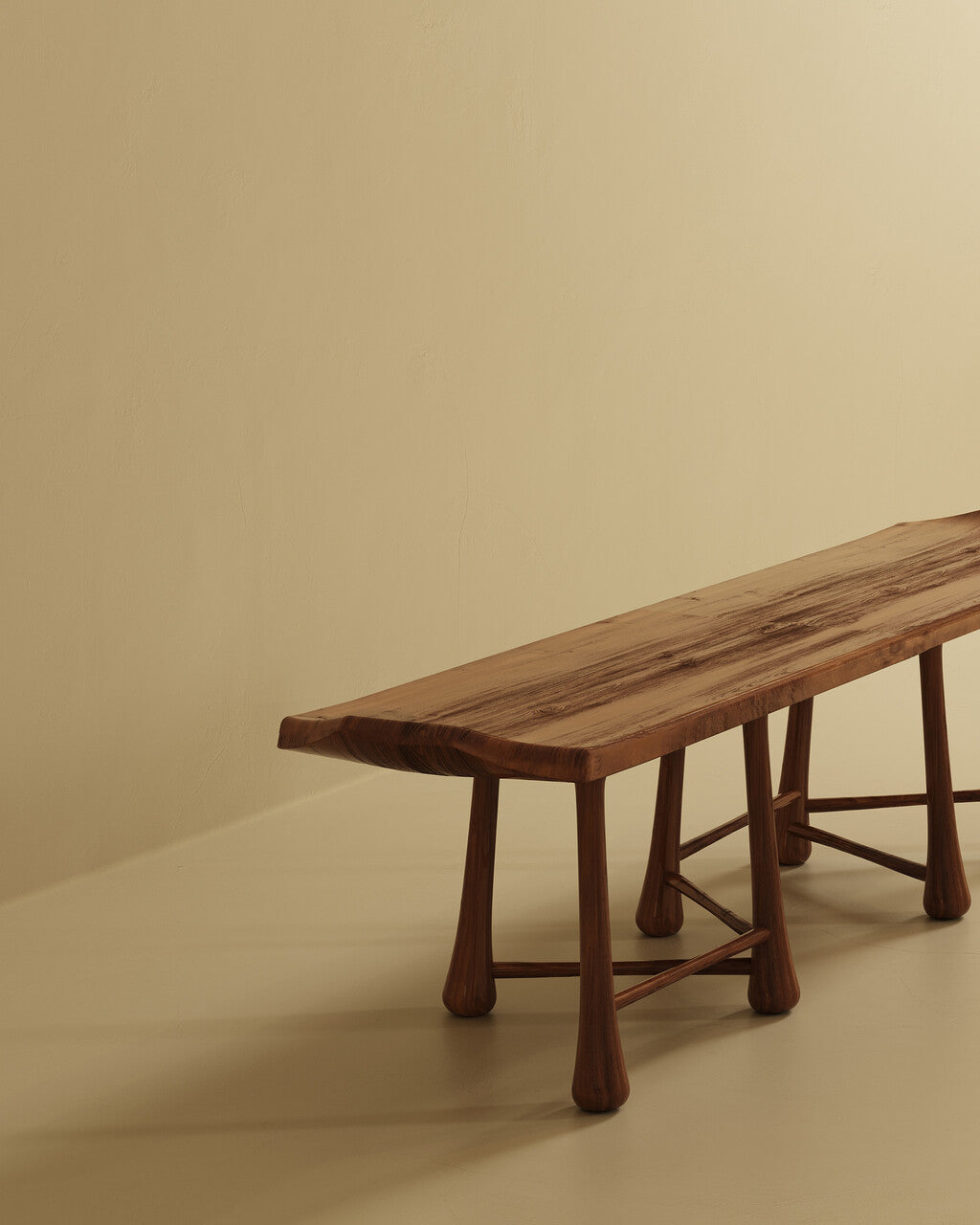 A long wooden bench with a flat rectangular seat and multiple rounded legs, photographed at an angle against a plain wall and floor.