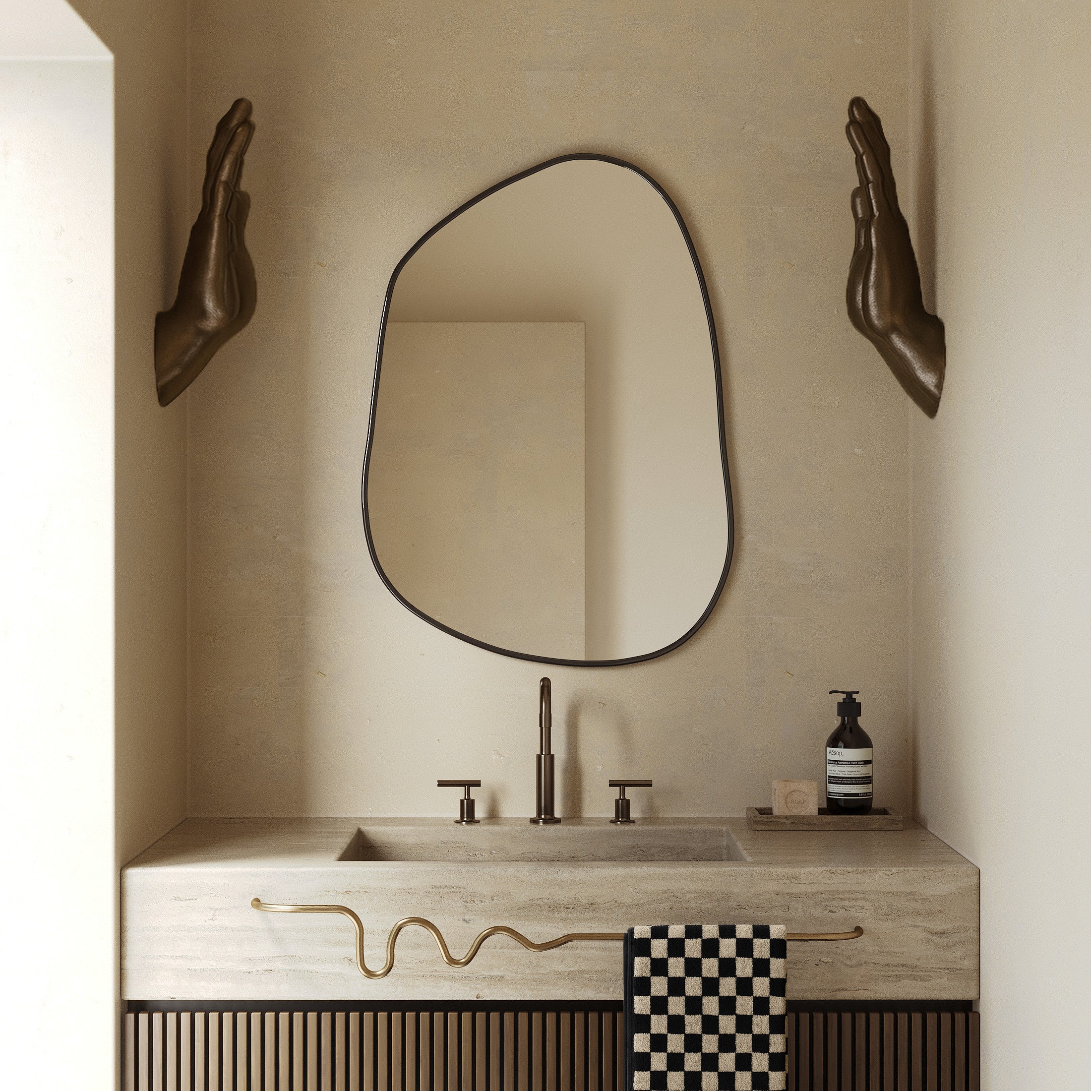 Organic-shaped mirror above a bathroom vanity with a wavy brass towel bar holding a checkered towel.