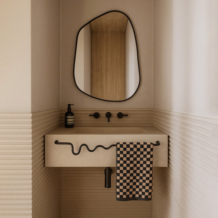 Black-framed organic mirror above a beige wall-mounted sink with a wavy towel bar and checkered hand towel.