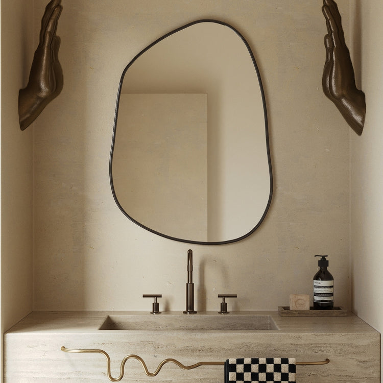 Asymmetrical wall mirror mounted above a stone bathroom vanity with bronze fixtures.