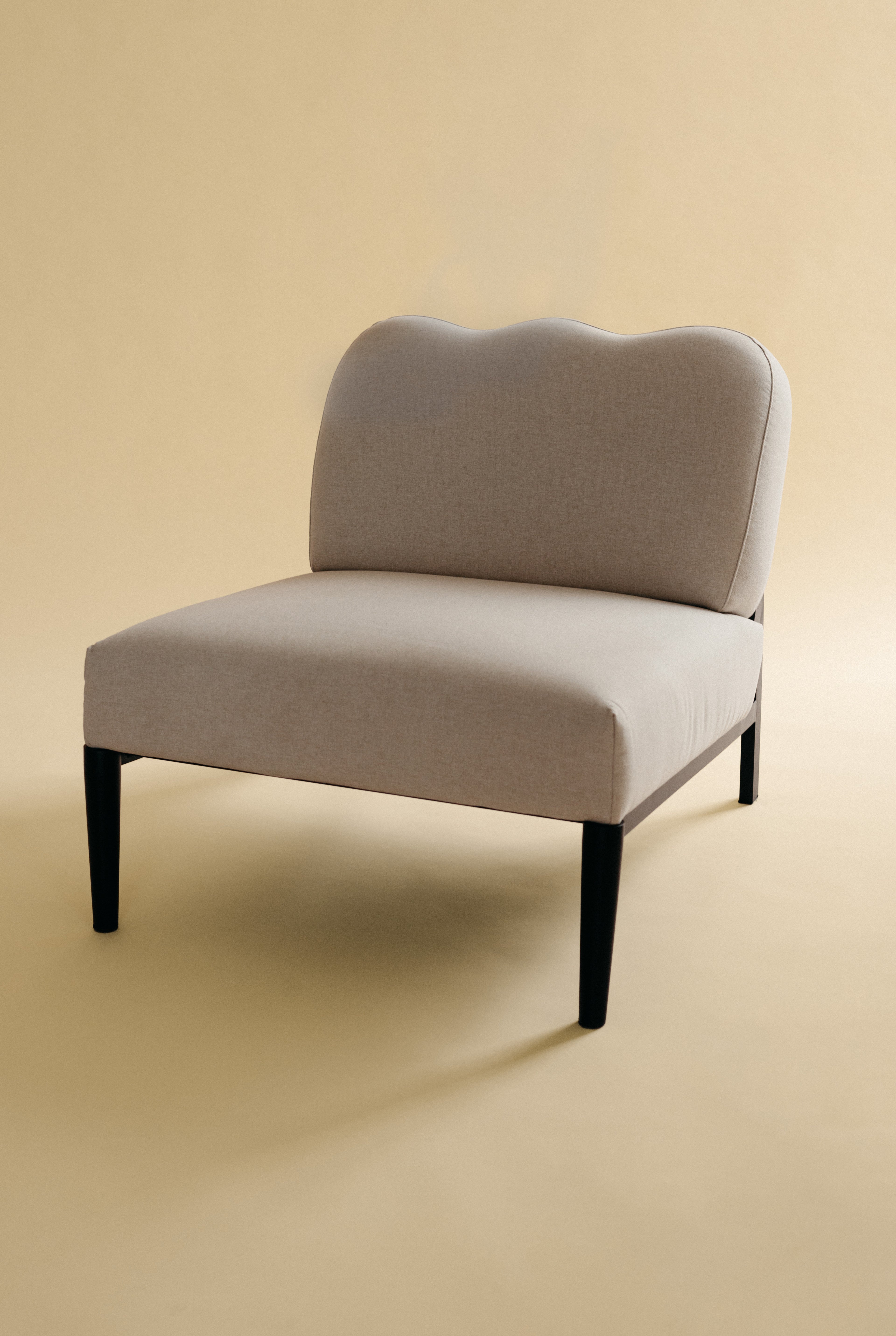 Beige linen upholstered accent chair with a curved backrest and black metal legs, angled view.