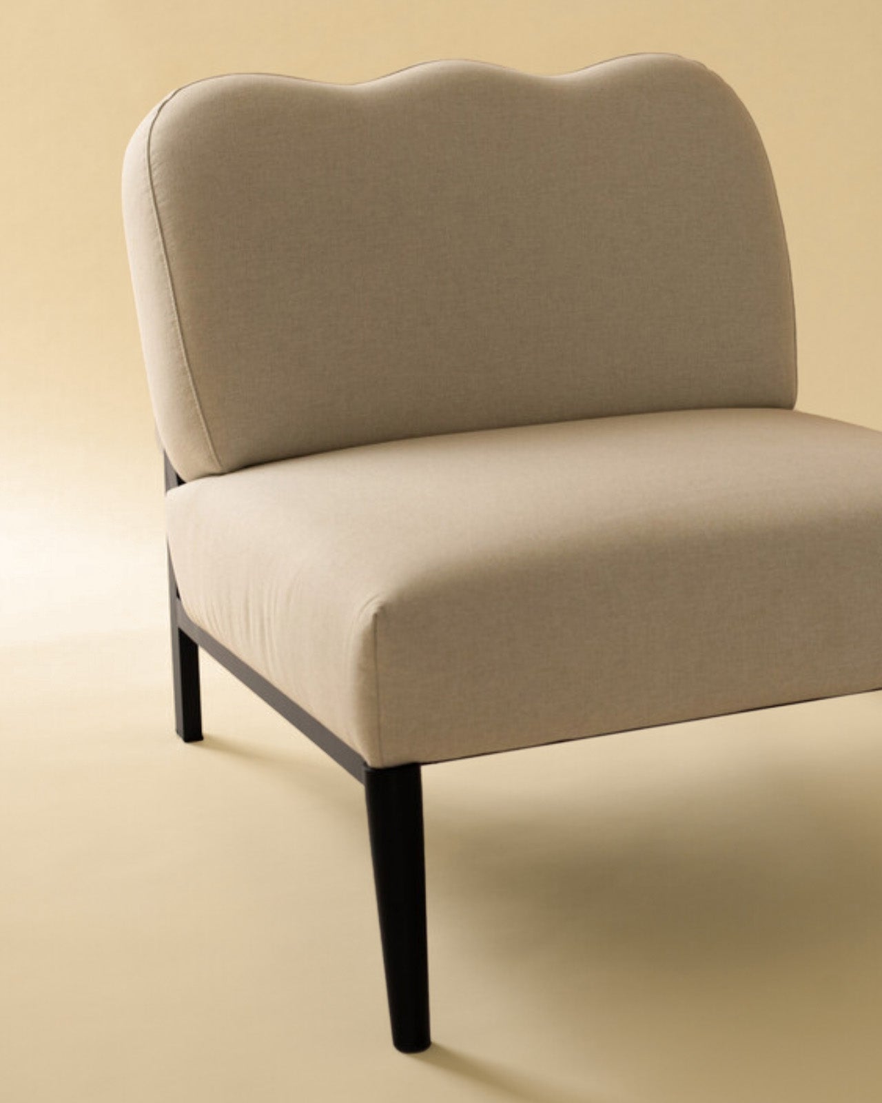 Detail view of a beige linen upholstered accent chair with a curved backrest and black metal leg.