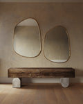 Two asymmetrical mirrors with organic shapes and thin brass-colored frames mounted side by side above a wooden bench.