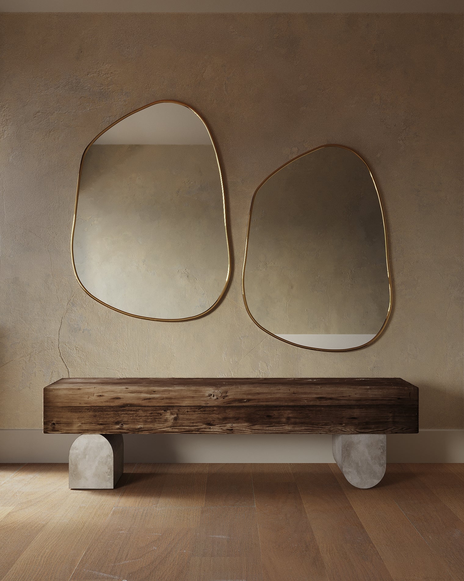 Two asymmetrical mirrors with organic shapes and thin brass-colored frames mounted side by side above a wooden bench.