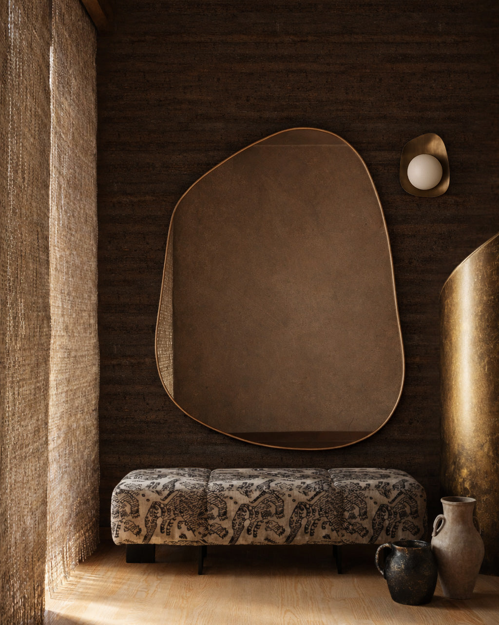 Irregular-shaped wall mirror mounted above a patterned upholstered bench beside decorative vases and sculptural elements.