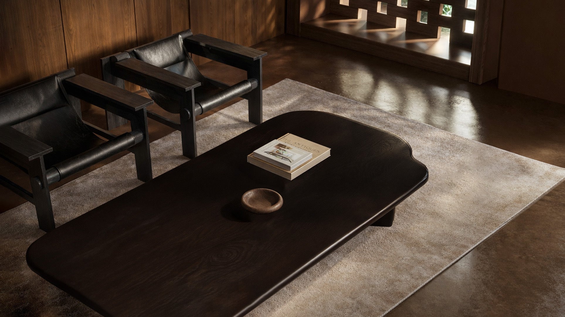 Dark wood coffee table with a book and small bowl on a light rug, beside two black leather chairs in a minimalist living room.