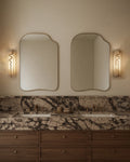 Two asymmetrical gold-framed wall mirrors mounted above a double vanity in a bathroom, with wall sconces on each side.