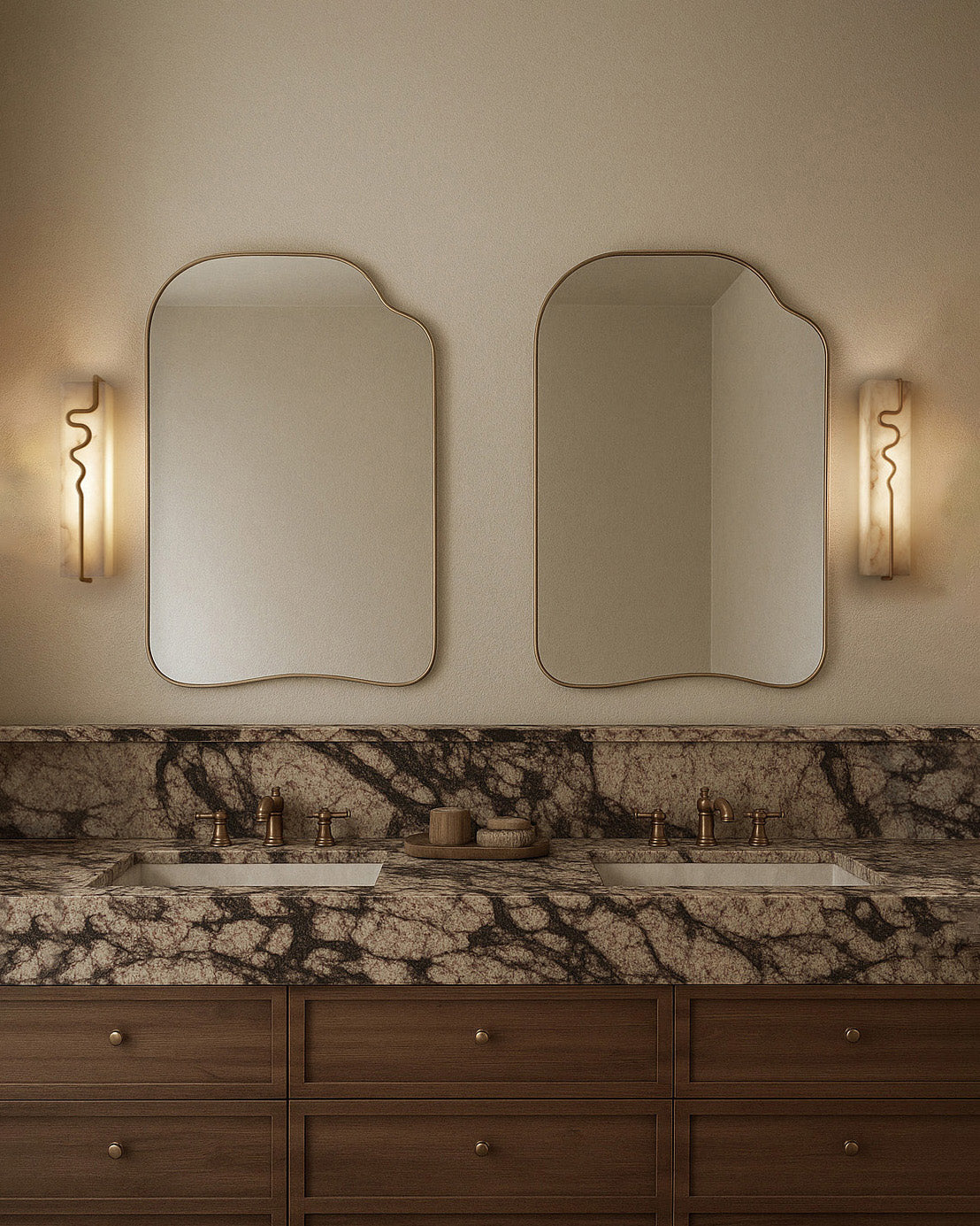 Two asymmetrical gold-framed wall mirrors mounted above a double vanity in a bathroom, with wall sconces on each side.