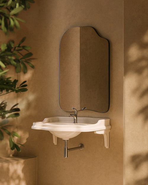 Asymmetrical wall-mounted mirror with a thin black frame above a wall-mounted sink in a bathroom setting.