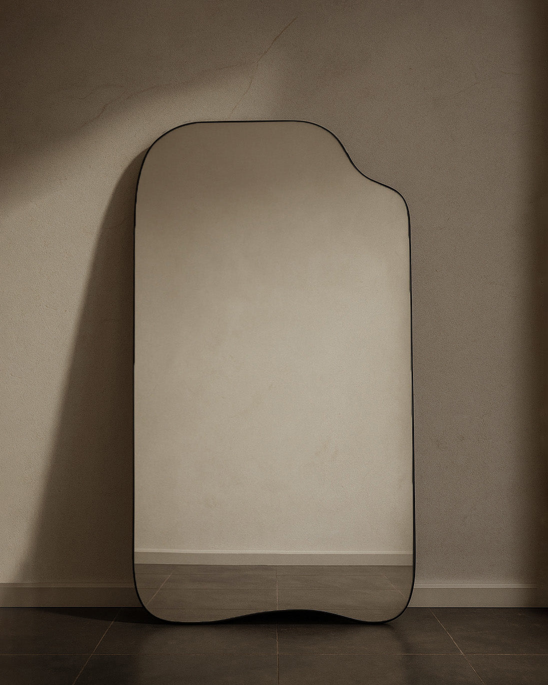 Asymmetrical full-length mirror with an organic shape and thin black frame, shown standing against a neutral wall on the floor.