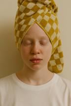 Model wearing a mustard yellow and white checkered towel wrapped around the head, highlighting the soft terry texture and geometric pattern.