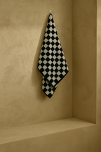 Black and white checkered towel hanging on a wall hook, showcasing the bold geometric pattern and textured terry fabric.