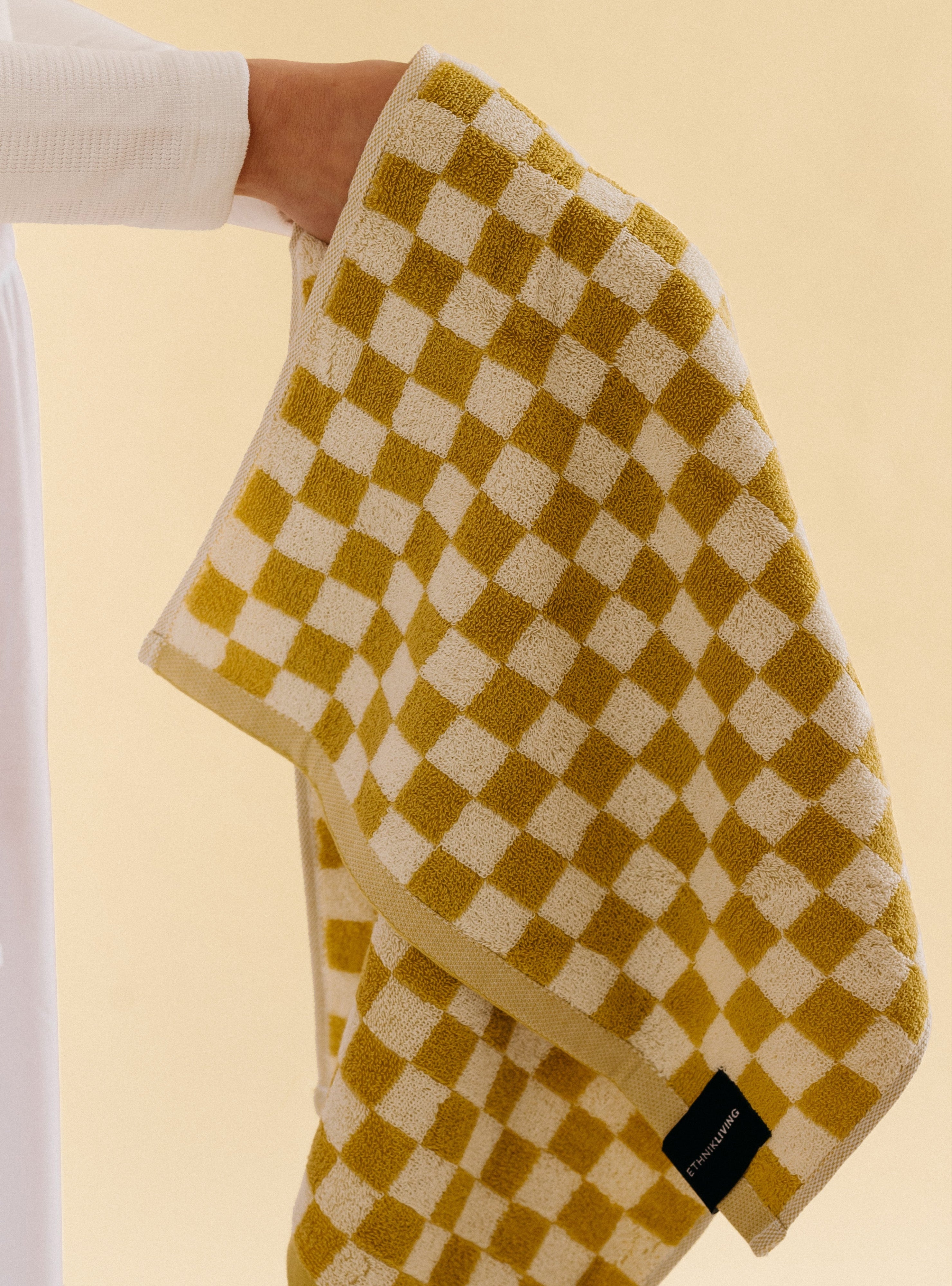 Mustard and white checkered towel with textured surface and woven brand label, photographed against a neutral background.