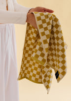 Hand holding a mustard yellow and white checkered towel, showing the soft terry texture, woven pattern, and finished edges against a neutral background.