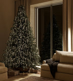 A Christmas tree decorated with clear glass icicle ornaments and warm white lights in a softly lit living room.