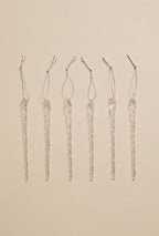 Six clear glass icicle ornaments with hanging loops arranged in a straight row on a neutral background.