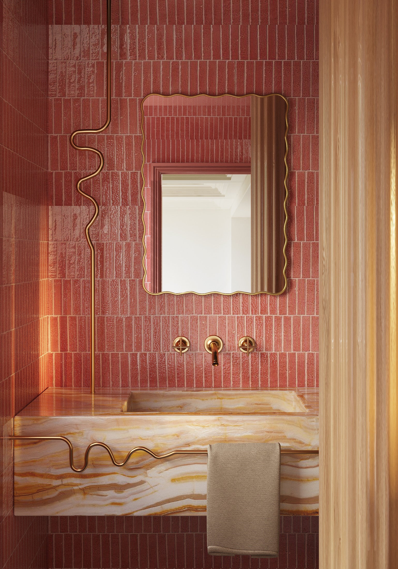 Rectangular mirror with a wavy brass frame above a bathroom sink, shown with pink tiled walls and brass faucet details.