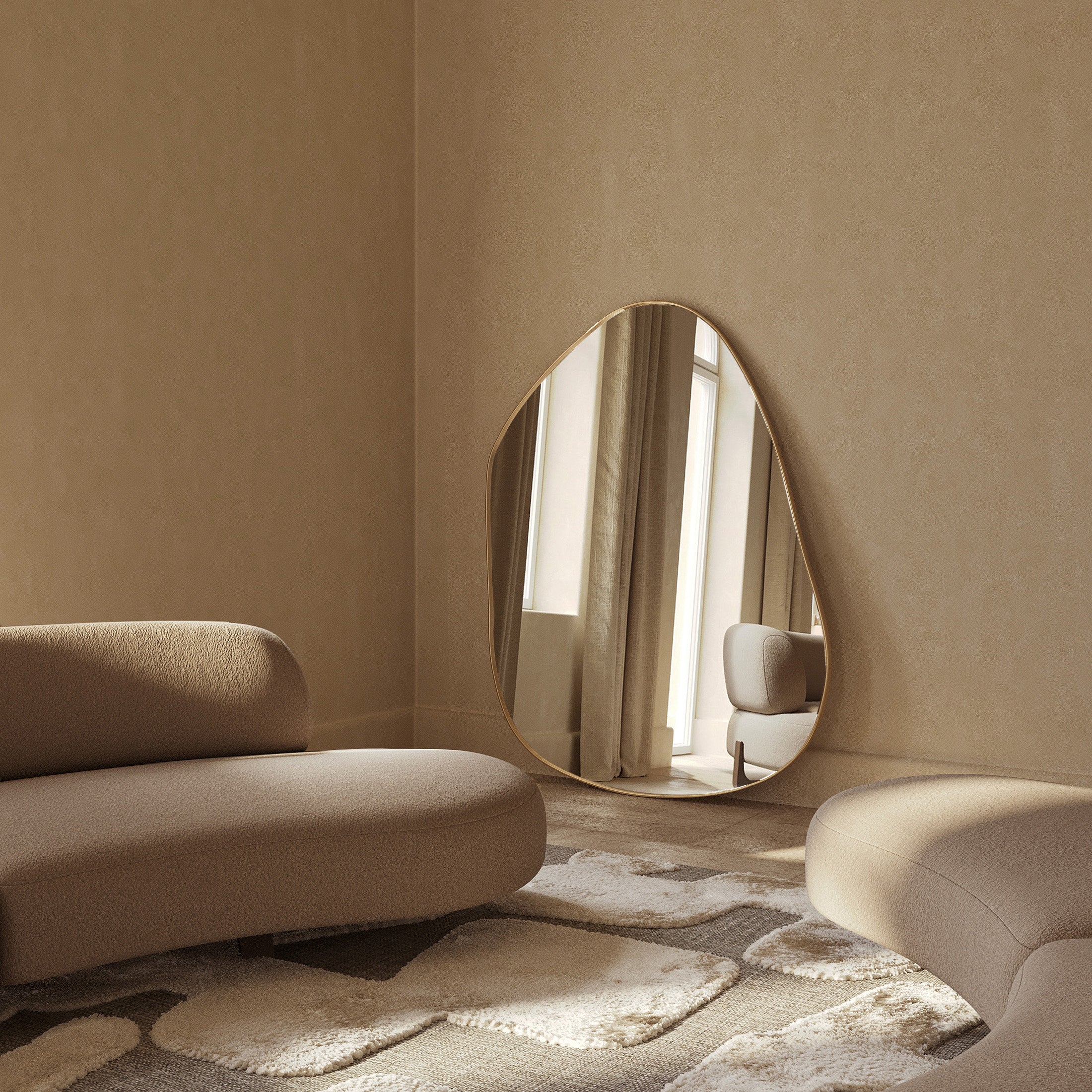 Asymmetrical brass-framed mirror leaning against a wall in a living space with upholstered seating and natural light.