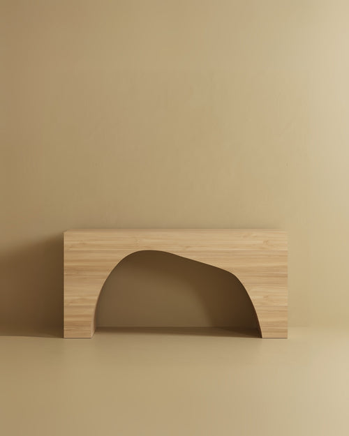 A rectangular console table made of wood veneer, featuring a smooth flat top and a wide arched opening at the base, positioned against a plain wall and floor.