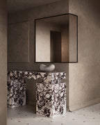 Marble console table with sculpted edges positioned against a wall with a square mirror above.