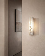 Alabaster wall sconce with brass detail casting warm light on a textured wall.