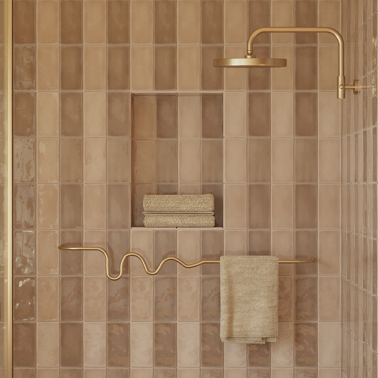 Brass wavy towel bar mounted on a tiled shower wall, holding a folded towel beneath a brass shower fixture.