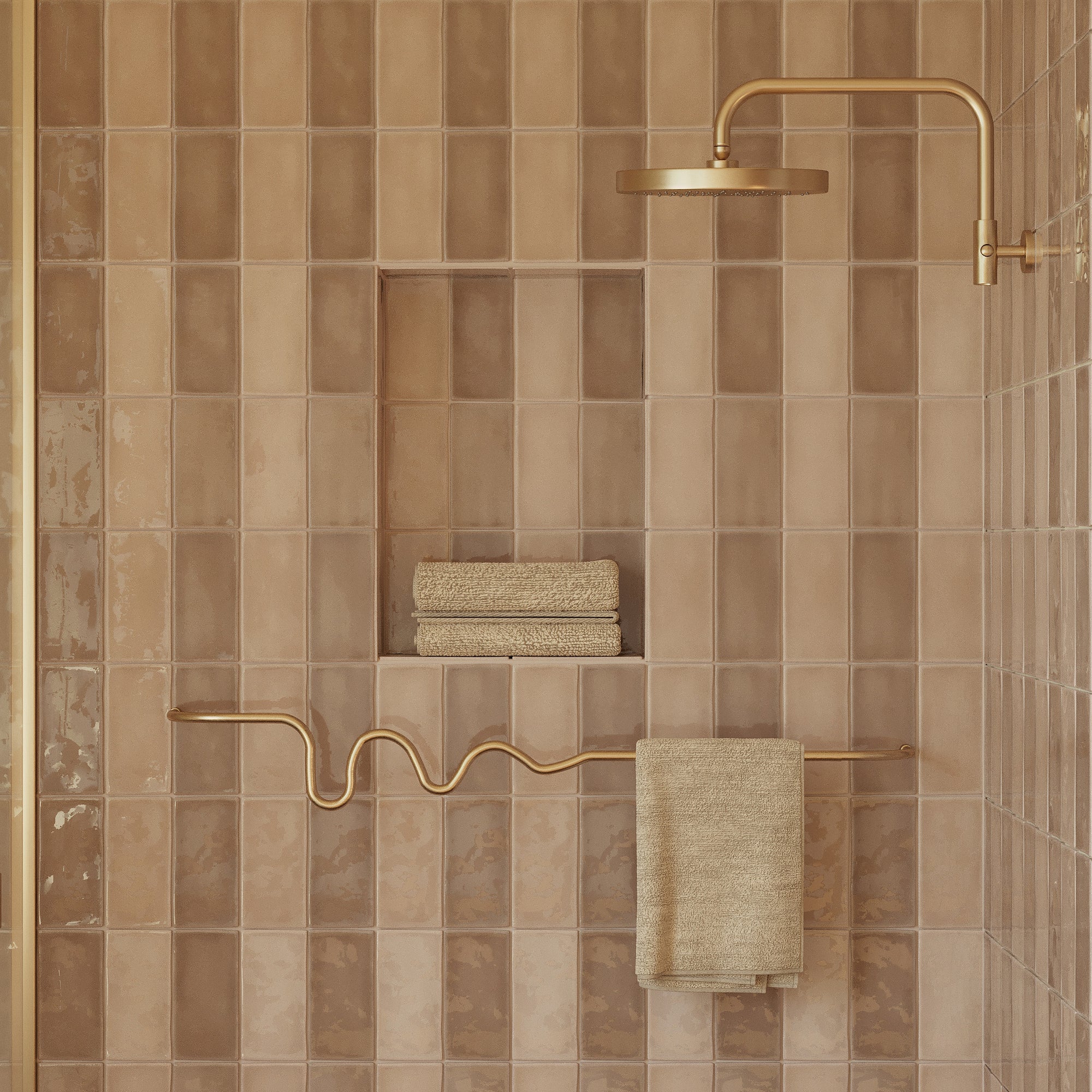 Brass wavy towel bar mounted on a tiled shower wall, holding a folded towel beneath a brass shower fixture.