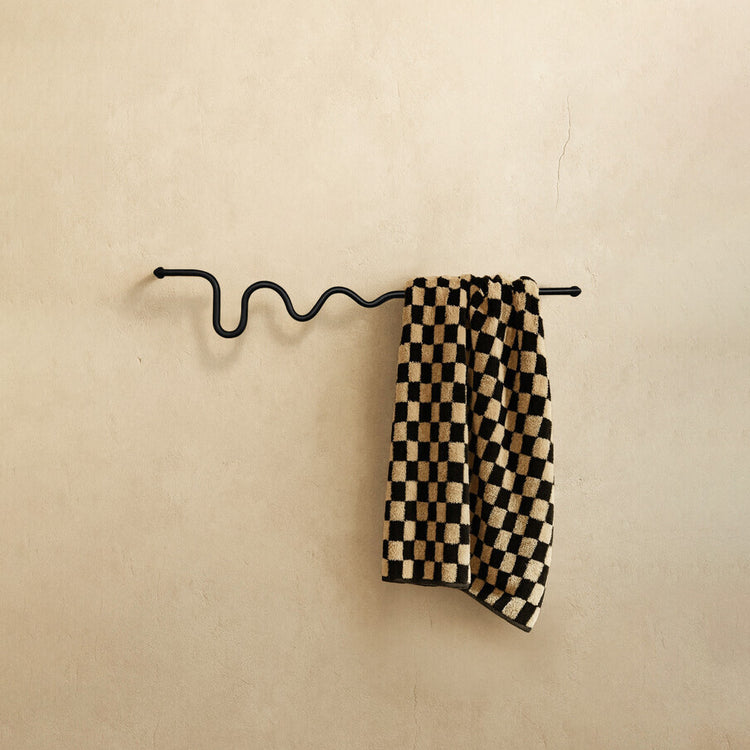Black wavy towel bar holding a checkered towel, shown against a neutral textured wall.