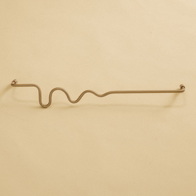 Brass-colored towel bar with a wavy organic shape, shown in a studio setting on a neutral background.